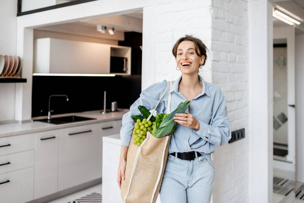Γυναίκα έρχεται στο σπίτι με τσάντα ψώνια γεμάτη φρέσκα τρόφιμα - Φωτογραφία, εικόνα