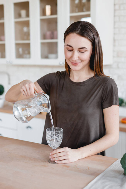 beautiful girl pours water into a glass in the kitchen - Zdjęcie, obraz