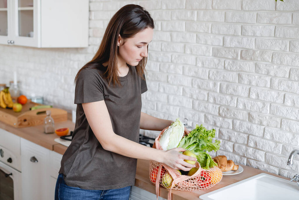 Dziewczyna parsuje worek z warzywami i owocami w kuchni - Zdjęcie, obraz