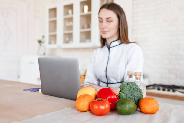 Médico nutricionista sentado na cozinha com um laptop
 - Foto, Imagem