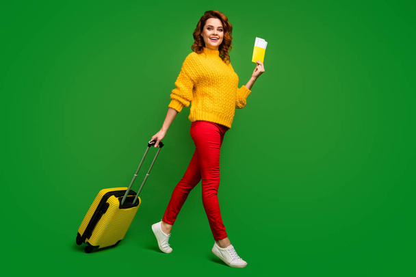 Πλήρης φωτογραφία προφίλ του σώματος της όμορφης κυρίας κατέχουν εισιτήρια περιοδεία στο εξωτερικό κυλιόμενη βαλίτσα με τα πόδια εγγραφή πτήσης φορούν κίτρινο πουλόβερ κόκκινα παπούτσια παντελόνι απομονωμένο πράσινο χρώμα φόντο - Φωτογραφία, εικόνα