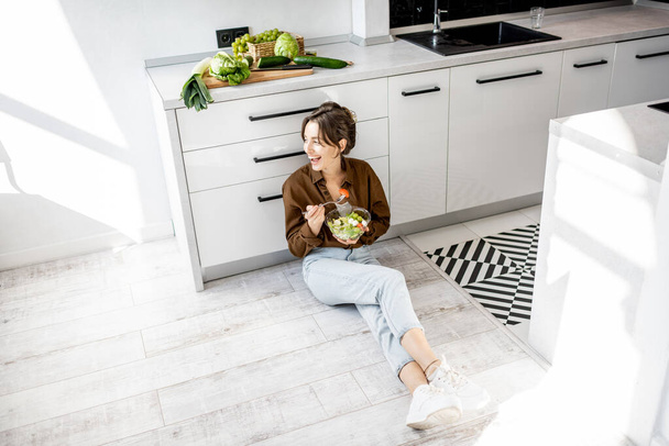Mulher com comida saudável no chão da cozinha
 - Foto, Imagem