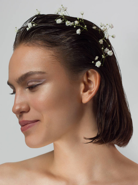 Close up portrait of a face with beautiful skin and nude makeup, eyeliner and long eyelashes, puffy natural lips and white flowers. Fashion photography. Cosmetology and spa. Freshness of spring - Fotó, kép