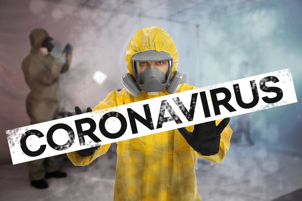 Man in chemical protective suit showing STOP gesture indoors. Prevention of virus spread - Fotografie, Obrázek