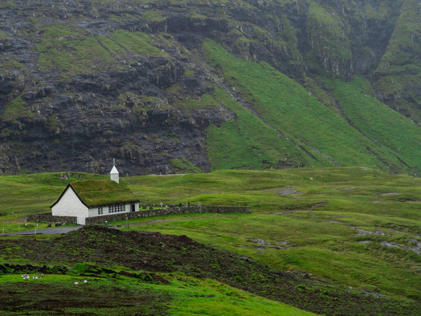Фарерские острова, Стреймой, Саксун. Вид на церковь и долину Саксуна. Белое здание с травяной крышей, стоящее из зеленых полей
. - Фото, изображение