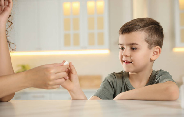 African-American woman giving vitamin pill to little boy in kitchen - Photo, image