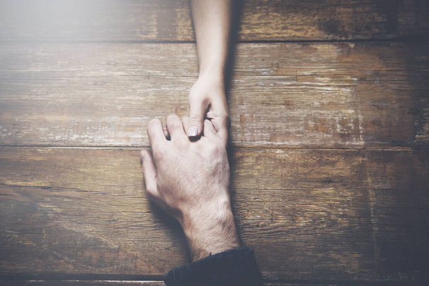 man and a woman holding hands at a wooden table - Foto, Imagen