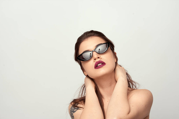 beautiful young girl with brown hair in fashionable glasses posing on a white background with bare shoulders, empty space for text - Foto, afbeelding