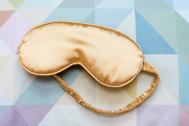 Golden sleeping eye mask on the bed, top view. Good night, flight and travel concept. Sweet dreams, siesta, insomnia, relaxation, tired, travel concept. Do not disturb, sleep, bedtime concept - Photo, Image
