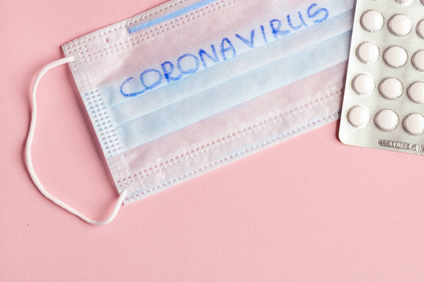 Wegwerp medische masker en blister met witte pillen liggen op een roze achtergrond - Foto, afbeelding