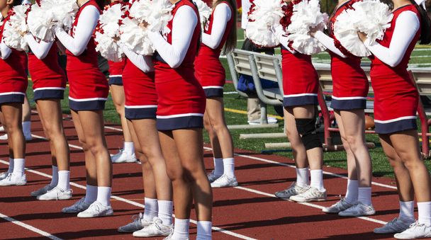 Animadoras de secundaria en uniformes rojos y blancos animan a los fans en un partido de fútbol de la escuela secundaria
. - Foto, imagen
