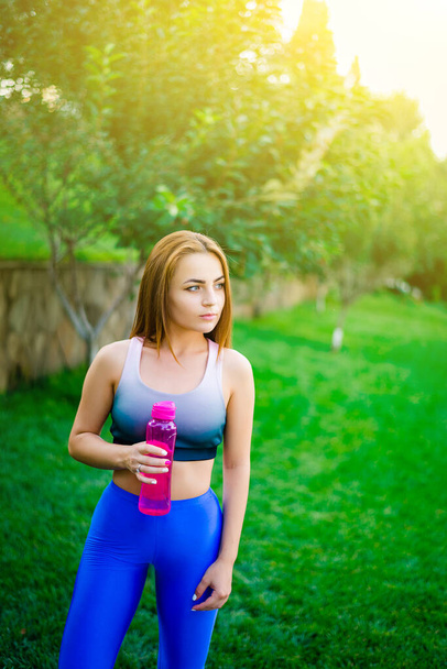 Fit junge Frau trinkt nach dem Training Wasser, die Großstadt ist im Hintergrund. - Foto, Bild