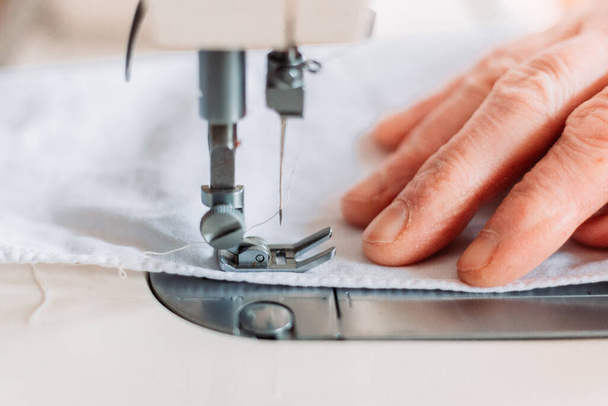 Close-up of womans hand sewing on the sewing mashine homemade medical mask. Shortage of medical equipment - Valokuva, kuva