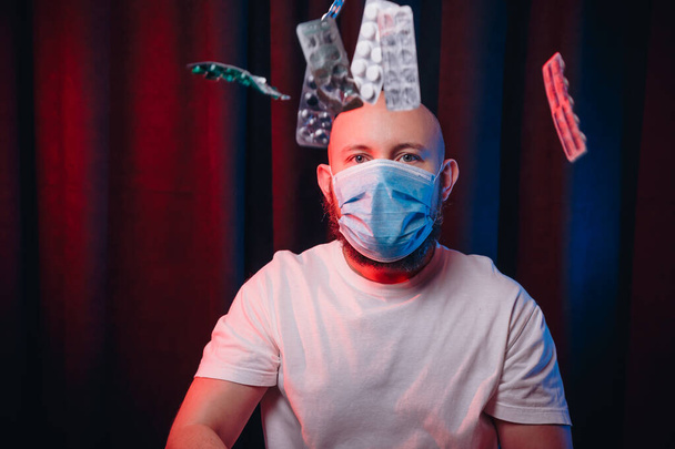 Man in gauze mask and flying medicines on dark red and blue background. Healthcare, respiratory illness prevention, prophylaxis of virus infections, COVID-19 concept. - Photo, Image