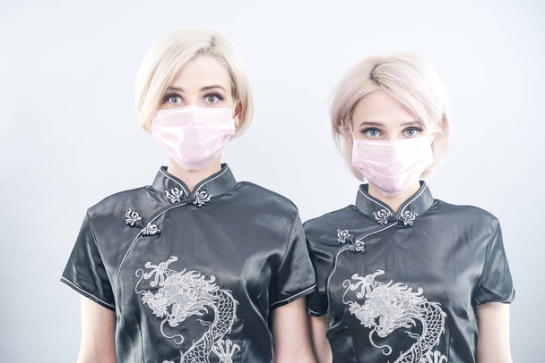 two European-looking women are dressed in black Chinese dresses and medical face masks. blonde girls do not keep a safe distance during coronovirus covid-19. 2 females in white photo Studio - Photo, Image