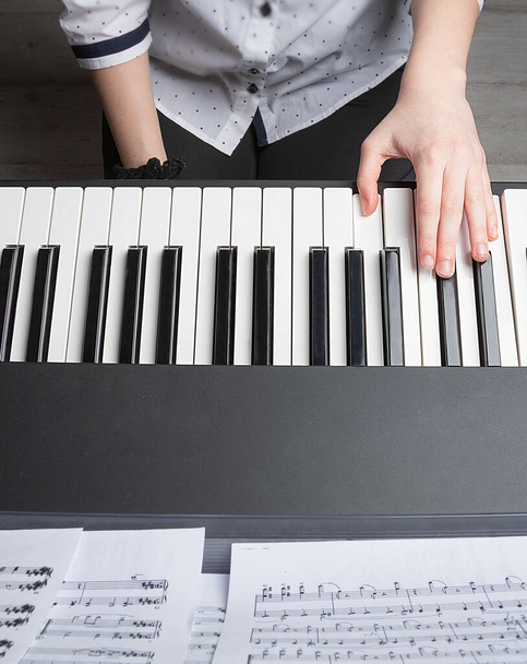 hrát na klavír jednou rukou. Dívčina levá ruka na klavírních klávesách, pohled shora. Hudební lekce. Zůstaň doma. - Fotografie, Obrázek