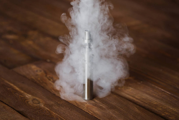 Electronic cigarette on a wooden table. Smoke. - 写真・画像