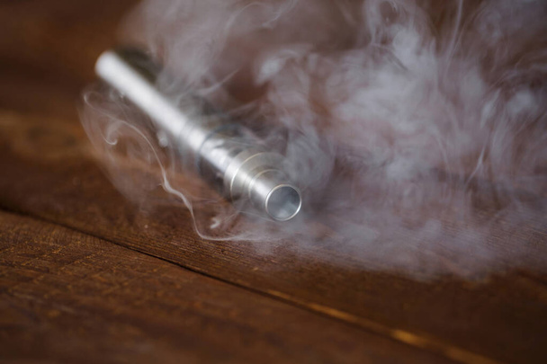 Electronic cigarette on a wooden table. Smoke. - 写真・画像