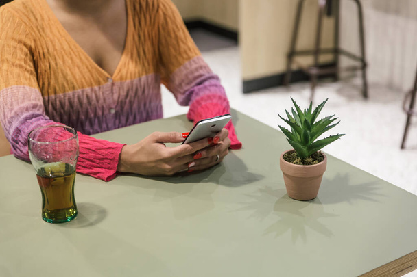 Egy nő karjainak látványa, amint gépel valamit a mobilján az asztalon egy kávézóban. - Fotó, kép