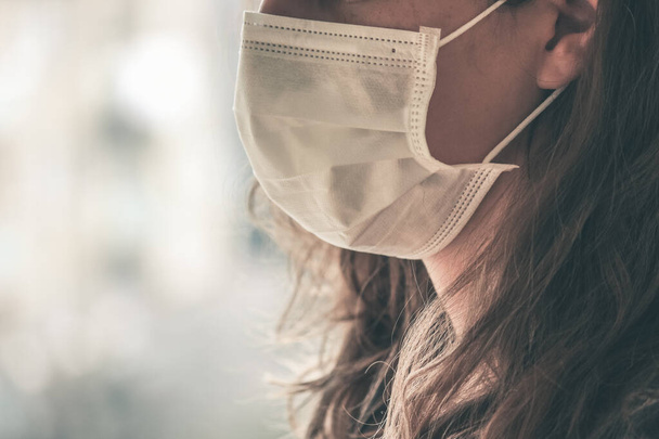 Αγνώριστη λευκή γυναίκα που φοράει λευκή μάσκα προσώπου για την πρόληψη μόλυνσης. Συγκεντρώσου στο μπροστινό μέρος του προσώπου, θολό φόντο. Coronavirus, καραντίνα COVID-19. Γιατρός, έννοια νοσοκόμα. - Φωτογραφία, εικόνα