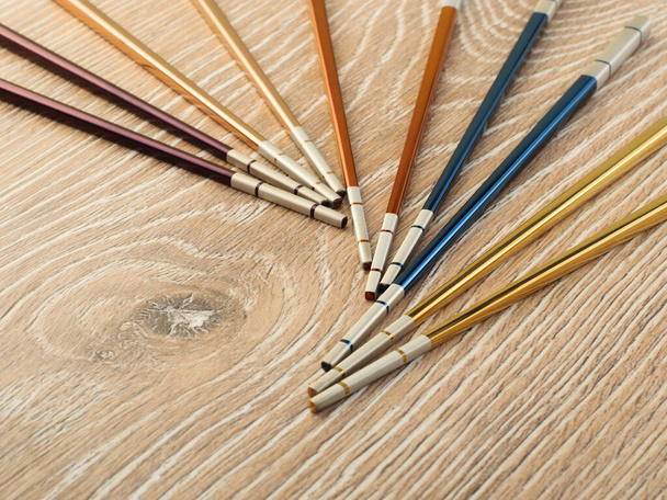 πολύχρωμα μεταλλικά ασιατικά chopsticks σε ξύλινο καφέ τραπέζι - Φωτογραφία, εικόνα