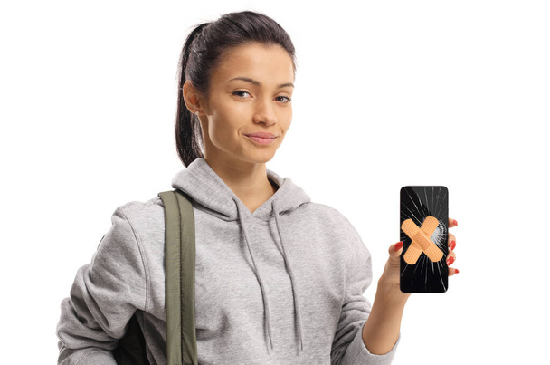 Young female holding a smartphone with a broken screen and aid bands on it isolated on white background - Photo, image