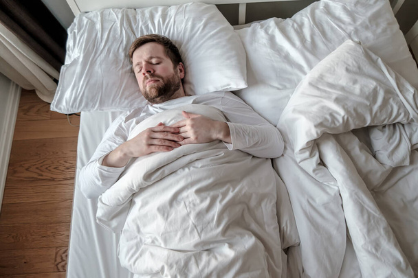 Caucásico barbudo hombre duerme tranquilamente en la cama con los brazos cruzados sobre su pecho
. - Foto, imagen
