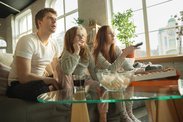 Rodzina spędza miło czas razem w domu, wygląda na szczęśliwą i podekscytowaną, je pizzę, ogląda mecz sportowy - Zdjęcie, obraz