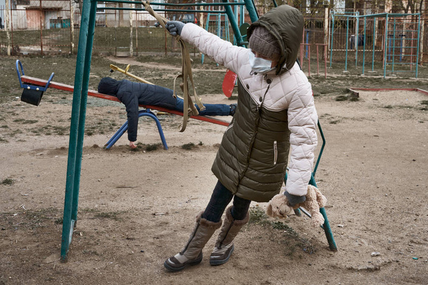 conceito de epidemia e quarentena - uma menina e um menino com uma máscara facial sozinhos no playground da cidade
 - Foto, Imagem