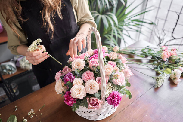 Έννοια ανθοπωλείου. Ανθοπωλείο γυναίκα δημιουργεί ρύθμιση λουλούδι σε ένα ψάθινο καλάθι. Όμορφο μπουκέτο από μικτά λουλούδια. Ωραία φρέσκια παρέα. Παράδοση λουλουδιών. - Φωτογραφία, εικόνα