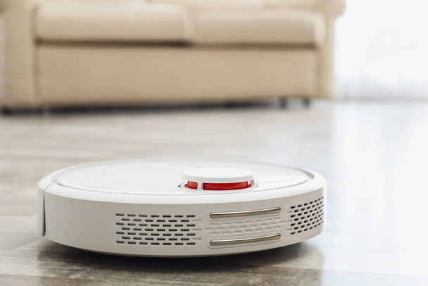 Modern robotic vacuum cleaner on floor in living room. Space for text - Photo, image