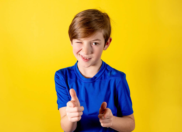 Close up boy winks. Hey, you. 9 years old boy winks with a smile. Photo of a boy on an orange background for the holiday, stock, sale - Zdjęcie, obraz