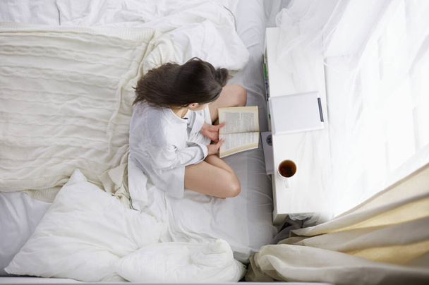 Woman sitting in bed reading a book and having breakfast - Foto, immagini