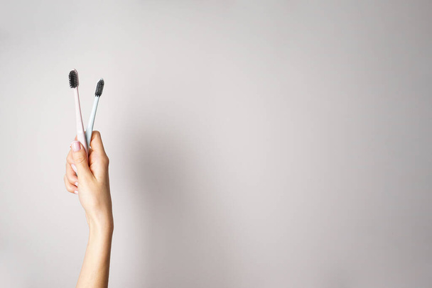 Colored toothbrushes with black bristles in the hands of a young woman on a gray background. Space for text, top view. - Photo, Image