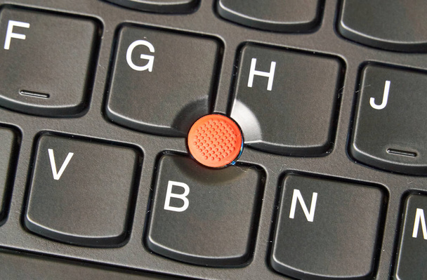 Trackpoint vermelho em um teclado de laptop. Um manípulo apontador é um pequeno joystick usado como um dispositivo apontador normalmente montado centralmente em um teclado de computador.
. - Foto, Imagem