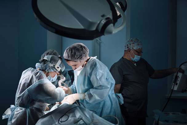 Στο χειρουργείο του νοσοκομείου. Μια διεθνής ομάδα επαγγελματιών χειρουργών και βοηθών εργάζεται σε ένα σύγχρονο χειρουργείο. Επαγγελματίες γιατροί γιορτάζουν έσωσε με επιτυχία ζωές. - Φωτογραφία, εικόνα