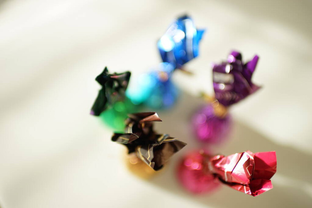 Cioccolatini in colorati involucri dai colori vivaci su un tavolo soleggiato, vista dall'alto, messa a fuoco selettiva
. - Foto, immagini