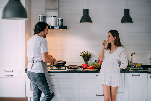 International Women's Day. Young couple in the morning in the kitchen at home. A man cooks a woman a festive breakfast on March 8 in a beautiful stylish kitchen. - Fotografie, Obrázek