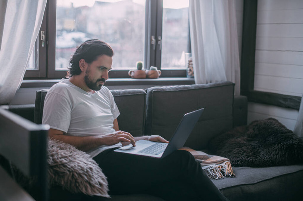Pracoviště doma. Muž pracuje doma na laptopu, přes den sedí na pohovce v obýváku a telefonuje. Práce z domova. - Fotografie, Obrázek