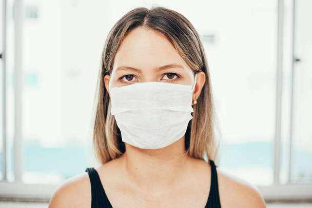 Portrait of woman wearing surgical mask at home. Covid-19, coronavirus and quarantine concept. - Valokuva, kuva