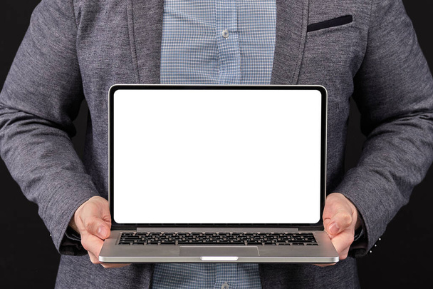 Un hombre con una chaqueta sosteniendo un portátil con espacio para copiar sobre un fondo negro. De cerca.
. - Foto, imagen