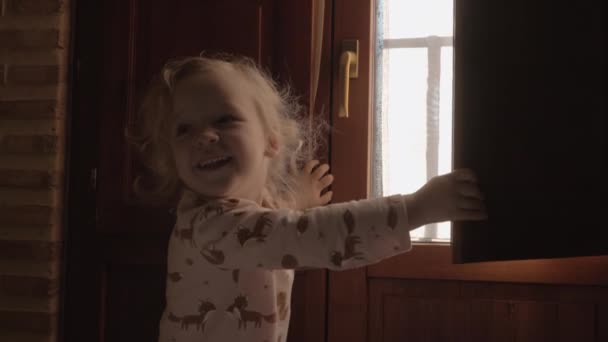 Little girl is happy with new day and opening shutters in the morning - Footage, Video