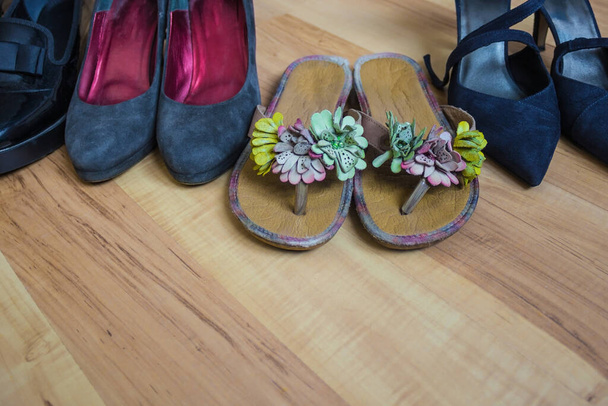 Dunkle, feminine, strenge Schuhe stehen in einer Reihe. Vor uns liegen helle, helle Schiefer. Warten auf Sommer, Urlaub, Freiheit. Holzboden, natürliches Licht. - Foto, Bild