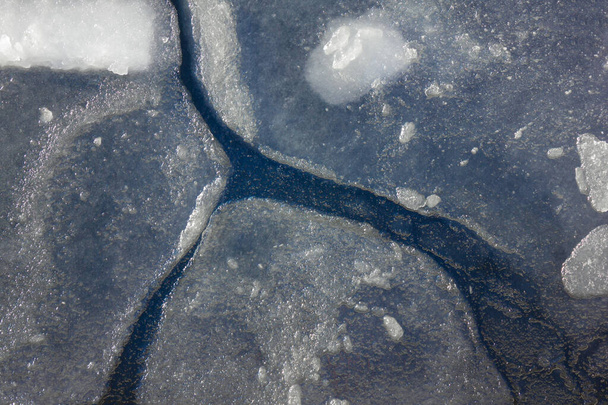 Gelo transparente, debaixo dele água escura. Na superfície de grandes rachaduras. No início da primavera, aquecimento. Iluminação solar, vista superior
. - Foto, Imagem