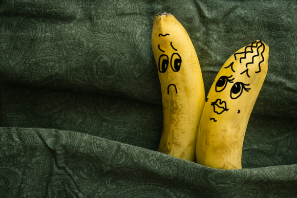 Ображаюча, сексуальна жінка і млявий, холодний чоловік. Два банани на темних аркушах, метафора. Чоловік і дружина, коханці. Картина створена автором.. - Фото, зображення
