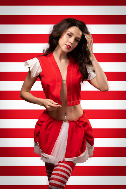 Concept vrouw in kostuum voor het feest. Full size portret van een aantrekkelijke mooie brunette in rood top, korte rok, gestreepte golf met krullende golven op een rood en wit geïsoleerde achtergrond - Foto, afbeelding