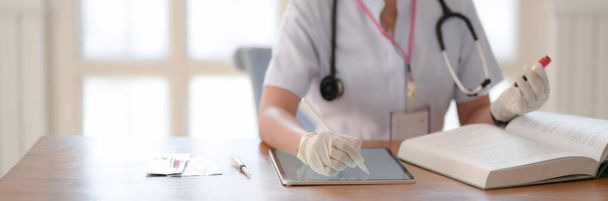 Close-up zicht van vrouwelijke arts met reageerbuis en op zoek naar informatie in een medisch boek tijdens het schrijven op digitale tablet  - Foto, afbeelding