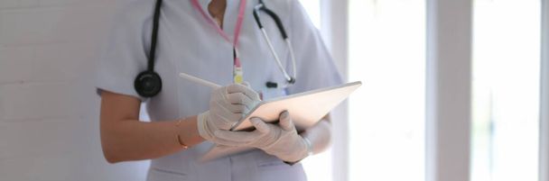 Vue latérale du médecin femme écrivant le dossier patient sur la tablette numérique dans la salle d'examen
 - Photo, image