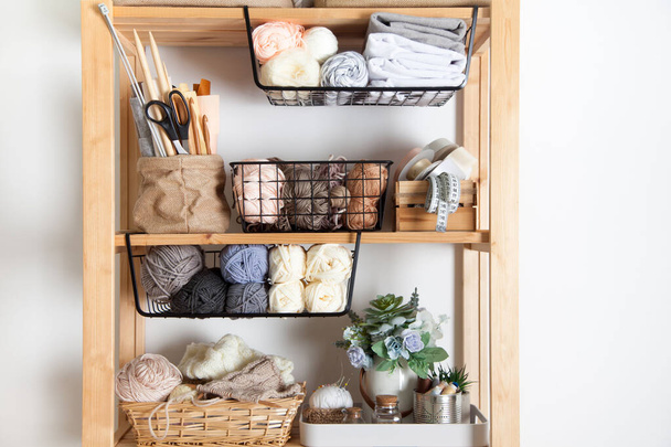 Different sewing supplies and yarn lie in baskets and stand on shelves on a wooden rack with a sewing machine on a white background. Concept of a seamstress and needlewoman workplace. Copyspace - Foto, imagen