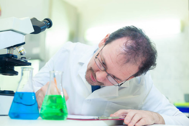 Chemicaliëngek. Een gekke wetenschapper voert experimenten uit in een wetenschappelijk laboratorium. Noteert onmiddellijk de resultaten van het onderzoek. COVID-19. COVID-coronavirus - Foto, afbeelding